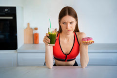 Front-view of a woman looking confused with a healthy smoothie and doughnut